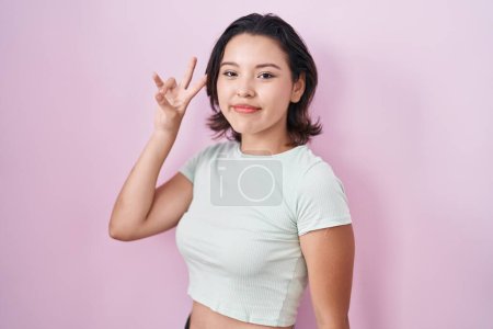 Téléchargez les photos : Hispanic young woman standing over pink background smiling looking to the camera showing fingers doing victory sign. number two. - en image libre de droit