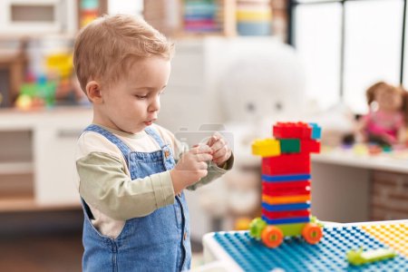 Téléchargez les photos : Adorable tout-petit jouant avec des blocs de construction debout à la maternelle - en image libre de droit