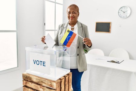 Foto de Mujer afroamericana mayor con bandera venezolana votando en colegio electoral - Imagen libre de derechos