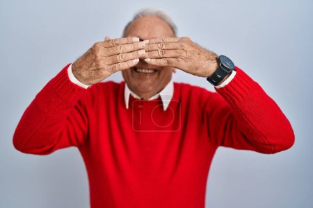 Téléchargez les photos : Senior man with grey hair standing over isolated background covering eyes with hands smiling cheerful and funny. blind concept. - en image libre de droit