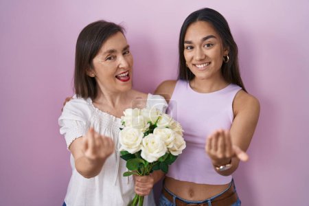 Foto de Hispanic mother and daughter holding bouquet of white flowers beckoning come here gesture with hand inviting welcoming happy and smiling - Imagen libre de derechos