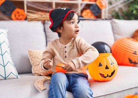 Téléchargez les photos : Adorable garçon hispanique ayant fête d'Halloween tenant panier de citrouille et bonbons à la maison - en image libre de droit