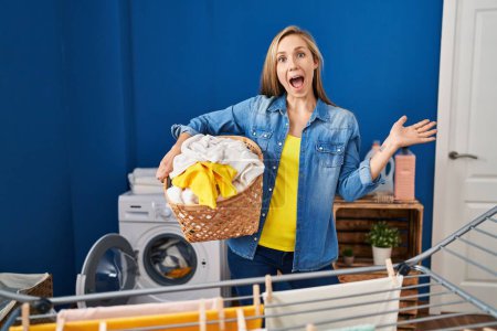 Photo for Young blonde woman holding laundry basket celebrating crazy and amazed for success with open eyes screaming excited. - Royalty Free Image