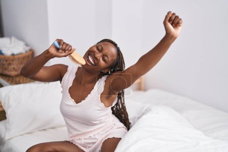 Téléchargez les photos : African american woman singing song using brush as a microphone at bedroom - en image libre de droit