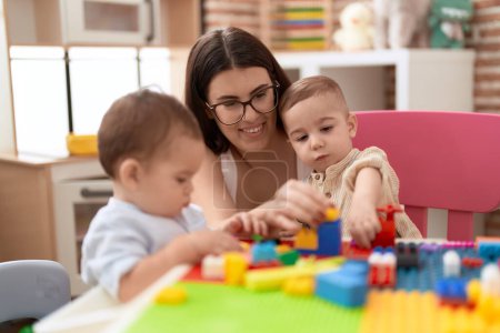 Téléchargez les photos : Enseignant et enfants d'âge préscolaire jouant avec des blocs de construction assis sur la table à la maternelle - en image libre de droit