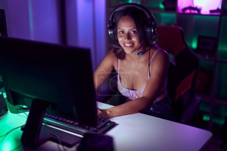 Foto de Young hispanic woman streamer smiling confident playing video game at gaming room - Imagen libre de derechos
