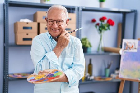 Téléchargez les photos : Senior grey-haired man artist smiling confident holding paintbrush and palette at art studio - en image libre de droit