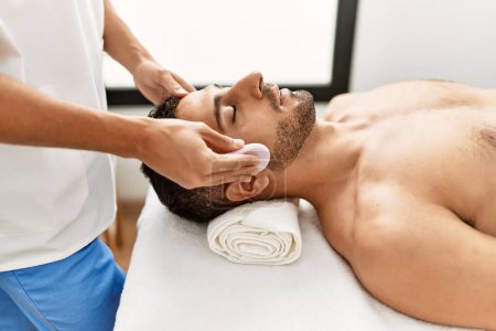 Foto de Dos hombres hispanos terapeuta y paciente con tratamiento facial limpieza de la cara en el centro de belleza - Imagen libre de derechos