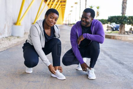 Téléchargez les photos : Couple homme et femme portant des vêtements de sport attachant des chaussures à la rue - en image libre de droit