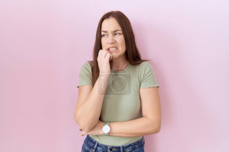 Photo for Beautiful brunette woman standing over pink background looking stressed and nervous with hands on mouth biting nails. anxiety problem. - Royalty Free Image