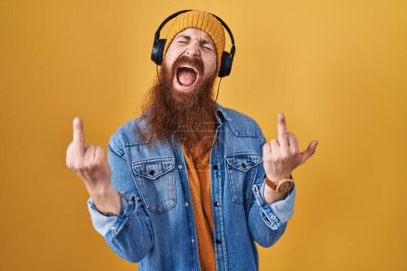 Téléchargez les photos : Caucasian man with long beard listening to music using headphones showing middle finger doing fuck you bad expression, provocation and rude attitude. screaming excited - en image libre de droit