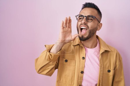 Téléchargez les photos : Young hispanic man standing over pink background shouting and screaming loud to side with hand on mouth. communication concept. - en image libre de droit