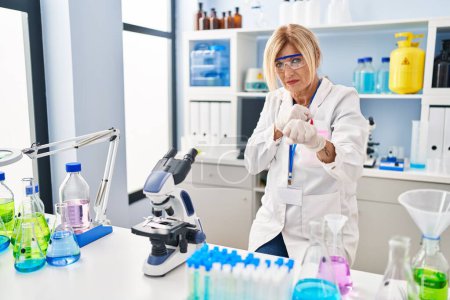 Foto de Middle age blonde woman working at scientist laboratory punching fist to fight, aggressive and angry attack, threat and violence - Imagen libre de derechos