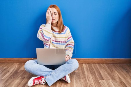 Téléchargez les photos : Young woman using laptop at home sitting on the floor yawning tired covering half face, eye and mouth with hand. face hurts in pain. - en image libre de droit