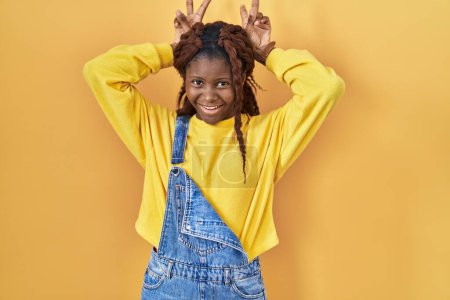 Foto de African woman standing over yellow background posing funny and crazy with fingers on head as bunny ears, smiling cheerful - Imagen libre de derechos