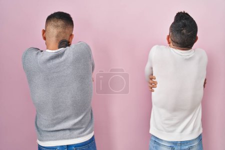 Foto de Pareja homosexual de pie sobre fondo rosa abrazándose feliz y positivo desde atrás. amor propio y cuidado personal - Imagen libre de derechos