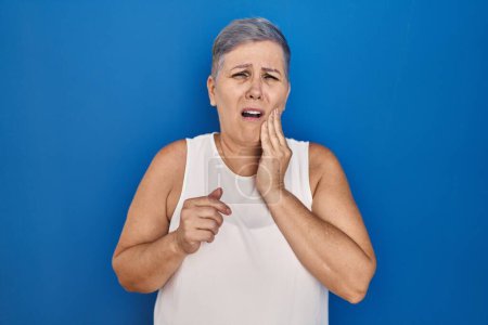 Photo for Middle age caucasian woman standing over blue background touching mouth with hand with painful expression because of toothache or dental illness on teeth. dentist - Royalty Free Image