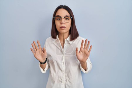Foto de Young hispanic woman standing over white background moving away hands palms showing refusal and denial with afraid and disgusting expression. stop and forbidden. - Imagen libre de derechos