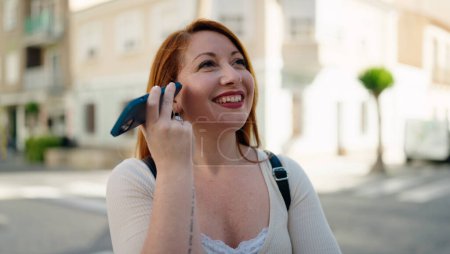 Foto de Young redhead woman smiling confident listening audio message by the smartphone at street - Imagen libre de derechos