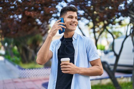 Téléchargez les photos : Jeune homme hispanique parlant sur le smartphone boire du café au parc - en image libre de droit