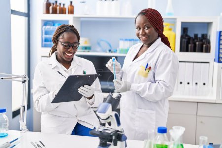 Téléchargez les photos : African american women scientist holding test tube writing on document at laboratory - en image libre de droit