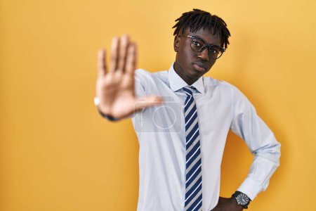 Photo for African man with dreadlocks standing over yellow background doing stop sing with palm of the hand. warning expression with negative and serious gesture on the face. - Royalty Free Image