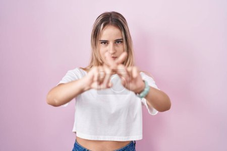 Téléchargez les photos : Jeune femme blonde debout sur fond rose expression de rejet croisement des doigts faisant signe négatif - en image libre de droit