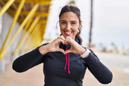 Foto de Young hispanic woman wearing sportswear doing heart symbol with hands at street - Imagen libre de derechos