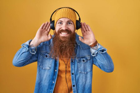 Photo for Caucasian man with long beard listening to music using headphones trying to hear both hands on ear gesture, curious for gossip. hearing problem, deaf - Royalty Free Image