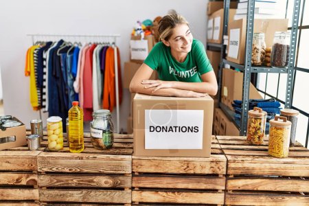 Téléchargez les photos : Jeune femme caucasienne portant un uniforme bénévole s'appuyant sur la boîte de dons au centre de bienfaisance - en image libre de droit