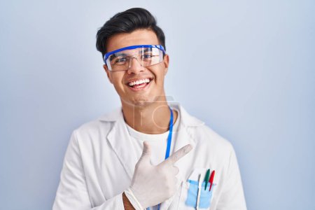 Foto de Hispanic man working as scientist cheerful with a smile of face pointing with hand and finger up to the side with happy and natural expression on face - Imagen libre de derechos