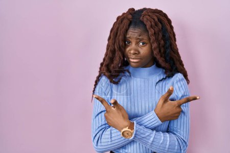 Photo for African woman standing over pink background pointing to both sides with fingers, different direction disagree - Royalty Free Image