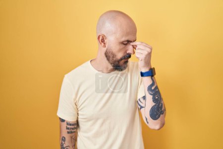 Foto de Hispanic man with tattoos standing over yellow background tired rubbing nose and eyes feeling fatigue and headache. stress and frustration concept. - Imagen libre de derechos
