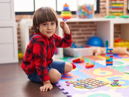 Foto de Adorable niño jugando con matemáticas juego sentado en el suelo en el jardín de infantes - Imagen libre de derechos
