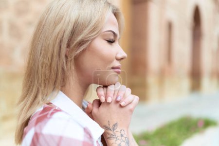 Foto de Young blonde woman praying with closed eyes at street - Imagen libre de derechos