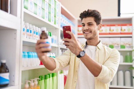Téléchargez les photos : Young hispanic man customer make photo by smartphone to medicine bottle at pharmacy - en image libre de droit