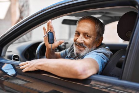 Téléchargez les photos : Homme âgé aux cheveux gris souriant confiant tenant la clé de la nouvelle voiture dans la rue - en image libre de droit