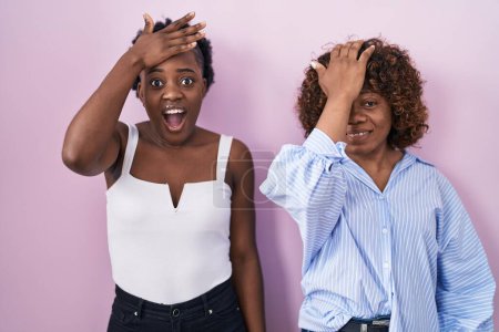 Téléchargez les photos : Deux femmes africaines debout sur fond rose surpris avec la main sur la tête pour erreur, rappelez-vous erreur. oublié, mauvais concept de mémoire. - en image libre de droit