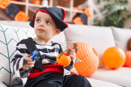 Foto de Adorable hispanic boy having halloween party holding pumpkin basket and car toy at home - Imagen libre de derechos