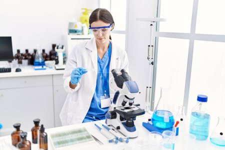 Photo for Young hispanic woman wearing scientist uniform using microscope at laboratory - Royalty Free Image