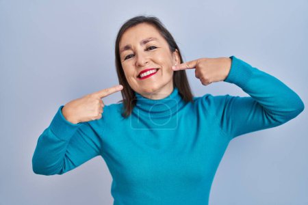 Photo for Middle age hispanic woman standing over isolated background smiling cheerful showing and pointing with fingers teeth and mouth. dental health concept. - Royalty Free Image
