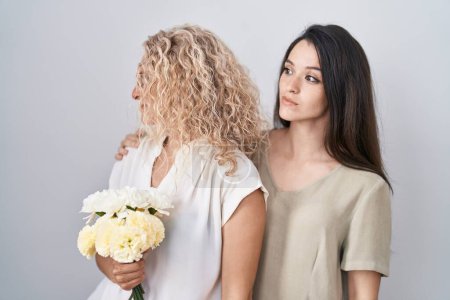 Téléchargez les photos : Mère et fille tenant bouquet de fleurs blanches regardant vers le côté, pose de profil relax avec visage naturel et sourire confiant. - en image libre de droit