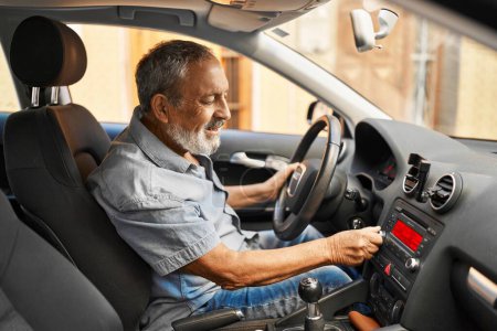 Foto de Senior grey-haired man sitting on car turning on radio at street - Imagen libre de derechos
