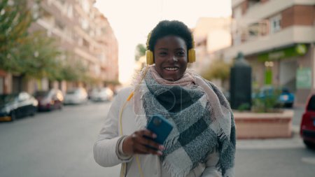 Téléchargez les photos : Jeune femme afro-américaine écoutant de la musique avec un smartphone dans la rue - en image libre de droit