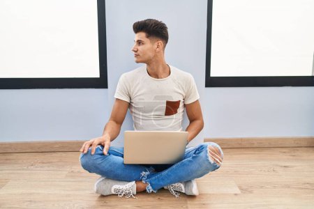Téléchargez les photos : Young hispanic man using laptop at home looking to side, relax profile pose with natural face and confident smile. - en image libre de droit