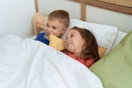 Téléchargez les photos : Adorable fille et garçon souriant confiant couché sur le lit dans la chambre - en image libre de droit