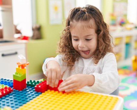 Foto de Adorable niño rubio jugando con bloques de construcción sentado en la mesa en el jardín de infantes - Imagen libre de derechos