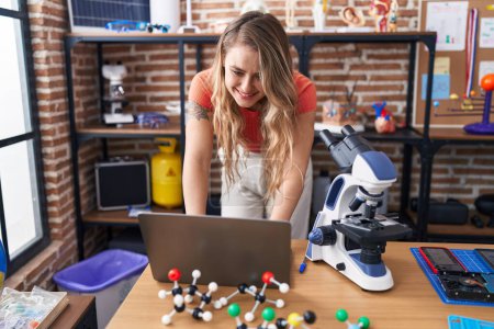 Photo for Young blonde woman teacher smiling confident using laptop at laboratory classroom - Royalty Free Image