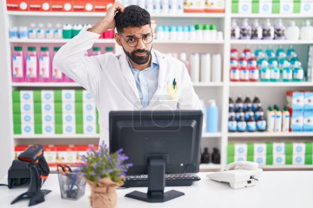 Photo for Hispanic man with beard working at pharmacy drugstore confuse and wonder about question. uncertain with doubt, thinking with hand on head. pensive concept. - Royalty Free Image
