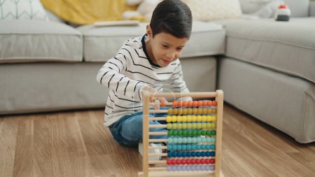 Foto de Adorable hispanic boy playing with abacus sitting on floor at home - Imagen libre de derechos